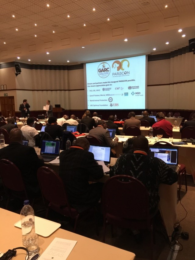 Delegates with laptops, sat at long tables in front of a speaker