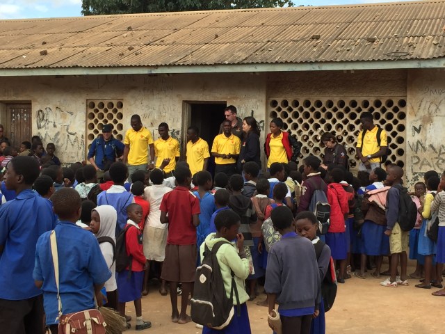 Group of schoolchildren crowding outside a building, in front of which adults in Mission Rabies stand