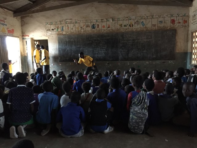 Schoolchildren sit on a classroom floor as a man in a Mission Rabies t-shirt speaks