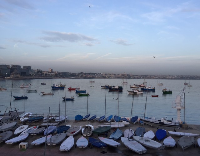 Small boats on the quayside, with more boats in the water behind and city on the other bankside in the background