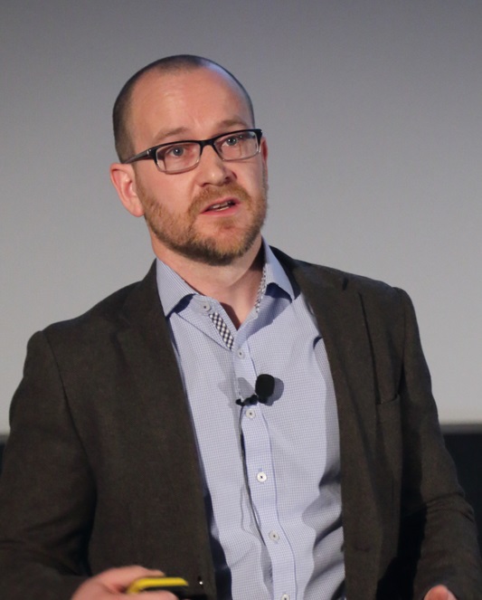 A man mid speech, wearing a microphone