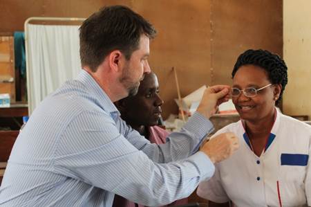 A man adjusts the glasses of a woman sat in front of him, whilst another man looks on