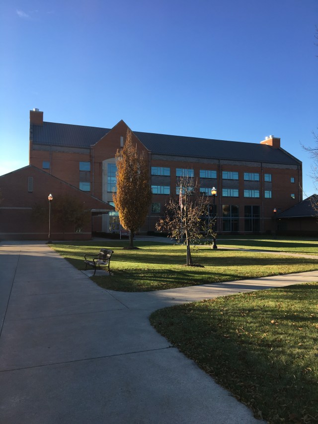 View of a large brick building, with trees, pathways and grass in front