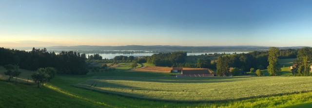 Hilltop view of green fields, farm buildings, trees and a stretch of water