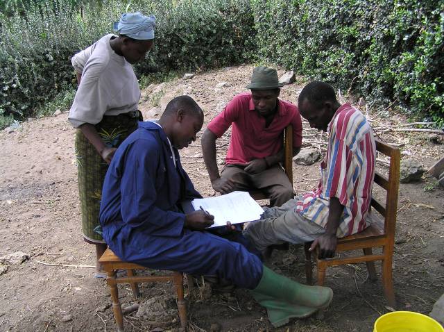 Herdsmen sitting in a group on chairs outside, writing up notes from sampling