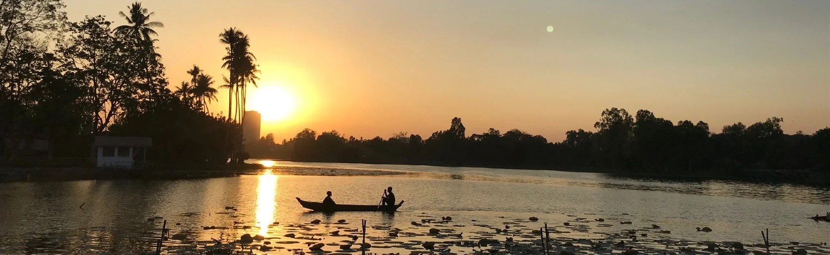 Innovation animal health banner image - Sunset over a stretch of water with silhouette of 2 men in a boat and palm trees on the riverside