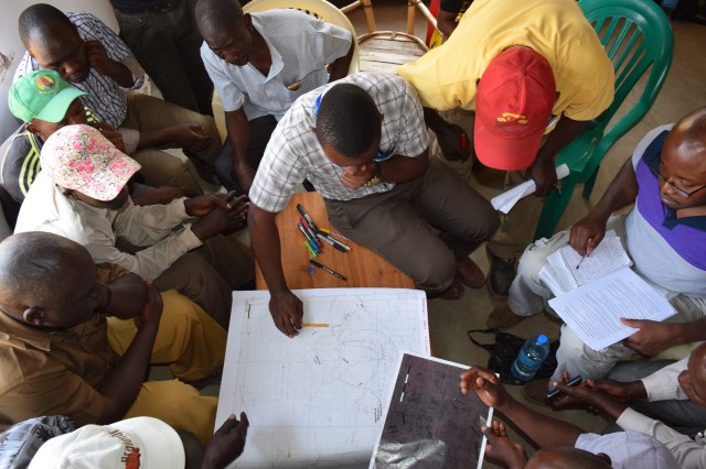 Focus On Tracking the movement of livestock - Group of men sat around a table studying a map