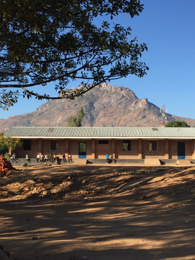 People sitting on a wall outside a building, with a mountain in the background